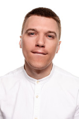 Fototapeta premium Charming handsome young man in a white shirt is making faces, while standing isolated on a white background