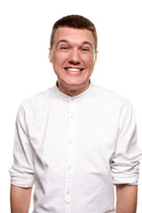 Charming handsome young man in a white shirt is making faces, while standing isolated on a white background