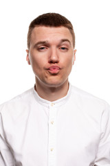 Fototapeta premium Charming handsome young man in a white shirt is making faces, while standing isolated on a white background