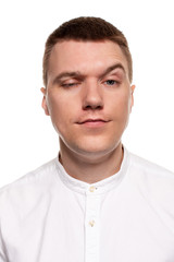 Obraz premium Charming handsome young man in a white shirt is making faces, while standing isolated on a white background