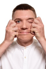 Charming handsome young man in a white shirt is making faces, while standing isolated on a white background