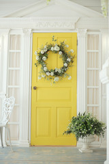 Beautifully decorated farmhouse look. Bright yellow door, a spring greenery wreath of flowers, a...