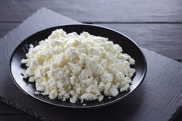 Cottage cheese on black slate board. Cottage cheese on black plate. Soft cheese for diet on black boards. Healthy dairy product for breakfast. Concept