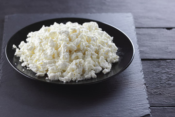 Cottage cheese on black slate board. Cottage cheese on black plate. Soft cheese for diet on black boards. Healthy dairy product for breakfast. Concept