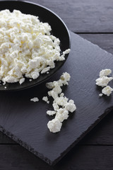 Cottage cheese on black slate board. Cottage cheese on black plate. Soft cheese for diet on black boards. Healthy dairy product for breakfast. Concept