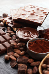 Melting chocolate or melted chocolate with a chocolate swirl and stack, chips and powder on black