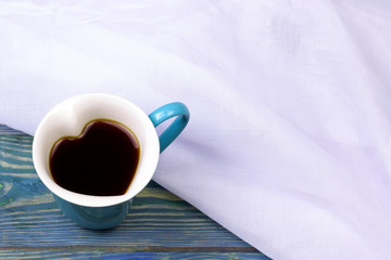 Heart shaped coffee cup on wooden background with white fabric. Love and romantic concept mockup.