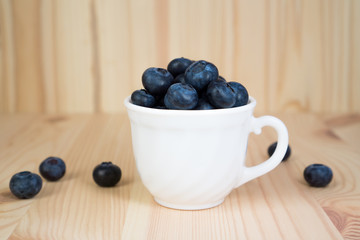 Blueberries in a white mug on a wooden background with copy space