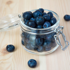 Blueberries in a glass jar on a wooden background. Square