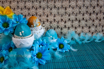 Wielkanocna kompozycja z niebieskimi pisankami, niebieskimi kwiatami oraz piórami na tle koronki © Monika