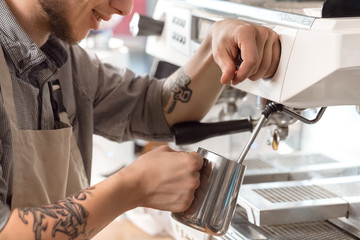 Made with love. Cropped closeup of a young barista smiling as he is preparing coffee on the coffee machine