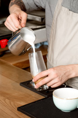 Sure you will love it. Vertical closeup of a barista pouring milk into the glass with coffee