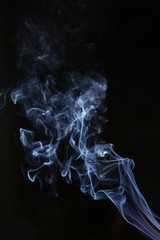 White and blue smoke on a black background. Sharp curls and smoke and out of focus.