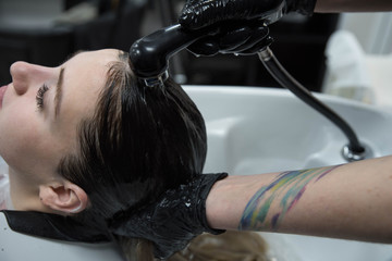 Fototapeta premium Beauty concept - Professional hairdresser applying shampoo, washes color paint off and massaging hair of a customer. Woman having her hair washed in a hairdressing beauty salon