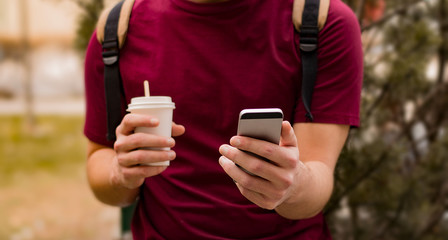 Man is using his mobile phone while holding a cup of coffee