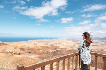 Woman looking at volcanic mountains and ocean landscape from Mirador de Morro Velosa viewpoint, Fuerteventura, Canary Islands, Spain