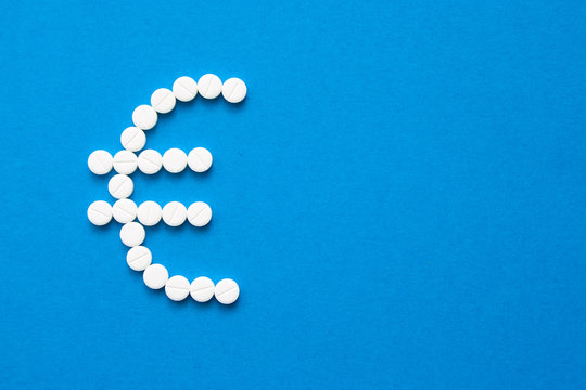 white pills in the shape of a euro are scattered on a blue background with copyspace