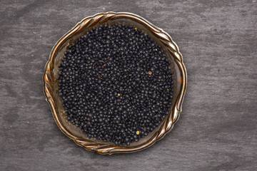 Lot of whole black lentils beluga variety in old iron bowl flatlay on grey stone