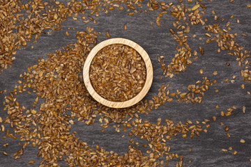Lot of whole raw bulgur grains with wooden bowl flatlay on grey stone