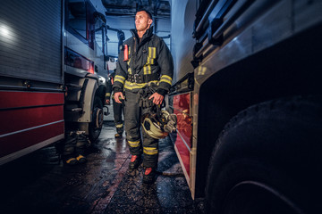 Fototapeta na wymiar Full-length portrait of two brave firemen in protective uniform walking between two fire engines in the garage of the fire station