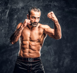 Fototapeta na wymiar Professional fighter showing kick fighting technique. Studio photo against a dark textured wall