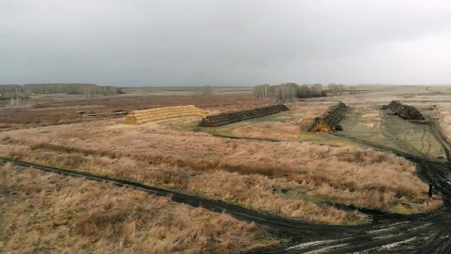 The view from the drone on the multicolored row of haystacks against the background of the autumn deserted rural landscape