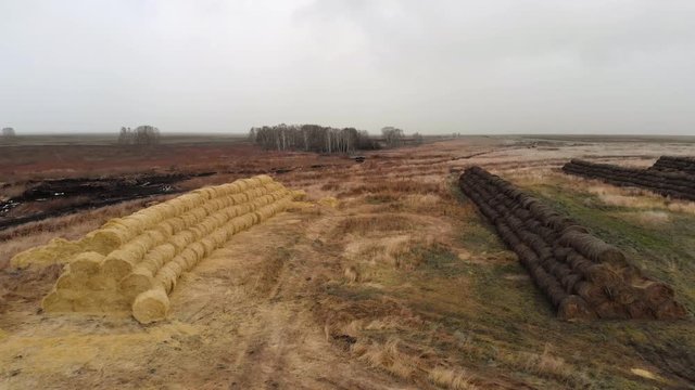 The view from the drone on the multicolored row of haystacks against the background of the autumn deserted rural landscape