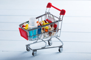 Shopping trolley cart with assorted medicine pills on light blue background. Creative idea for drugstore, online pharmacy, health behaviors