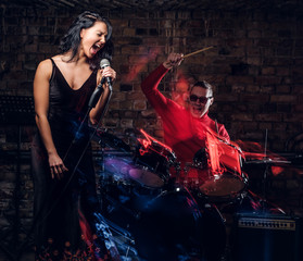 Fototapeta na wymiar Jazz band performance. Beautiful singer in elegant dress and drummer in a nightclub