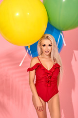 Young sexy slim woman in a red swimsuit with balloons in her hand is posing in a studio.