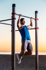 handsome man doing pull-ups at outside fitness park