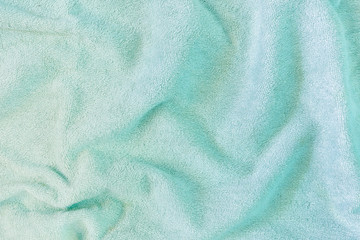 The texture of a crumpled terry towel. Folds and irregularities on the fabric. Green neutral background for layouts.