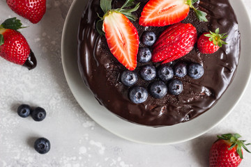 Cheesecake with raisin decorated with chocolate glaze and fresh strawberries and blueberries.