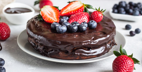 Cheesecake with raisin decorated with chocolate glaze and fresh strawberries and blueberries.