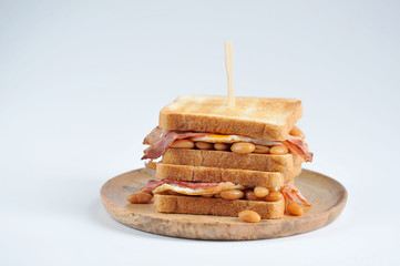 Sandwich with bacon, beans and fried egg on a wooden plate. Light background. Close-up.