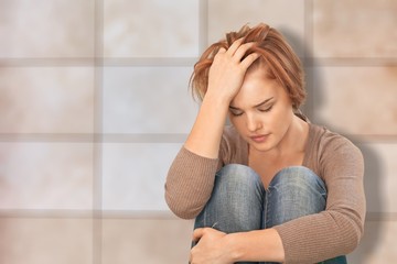 Worried woman sitting holding knees with arm on background