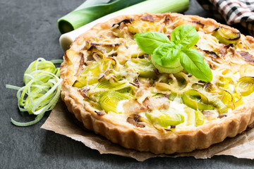 Leek tart with bacon and cheese on black stone background