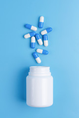 Blue pills, tablets and white bottle on blue background