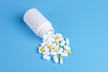 Medicine white and yellow pills or tablets drop out of the white bottle on blue background