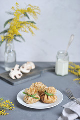 Pancakes in the shape of a bag stuffed with minced meat with mushrooms. In the background is a vase with a branch of mimosa, champignon slices, a can of sour cream. Gray background. Close-up.