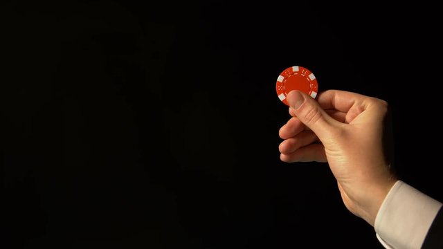 Hand in suit showing red chip against black background, successful poker bets