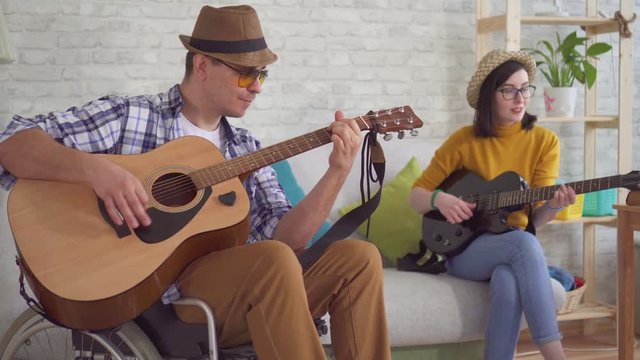 Young man is a disabled musician in a wheelchair player and a young woman in glasses and a hat playing the guitar