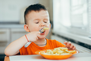 beautiful baby in orange t-shirt with orange plate eating fried French fries