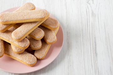 Savoyardi biscuits on pink plate over white wooden background, low angle view. Copy space.