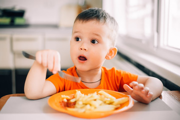 beautiful baby in orange t-shirt with orange plate eating fried French fries