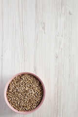 Overhead view, hulled sunflower seeds in a pink bowl over white wooden surface. Flat lay, top view, from above. Copy space.
