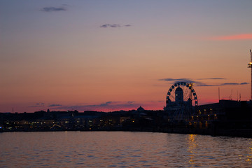 Obraz premium View of the embankment of Helsinki, the Ferris wheel, lights and the silhouette of the Cathedral of St. Nicholas from the Gulf of Finland at dusk on a bright summer night in the capital of Finland.