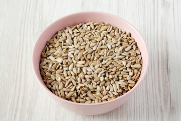 Dry hulled sunflower seeds in a pink bowl over white wooden surface, low angle view. Close-up.