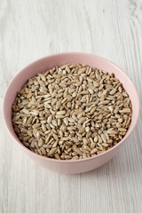 Dry hulled sunflower seeds in a pink bowl over white wooden background, low angle view. Closeup.