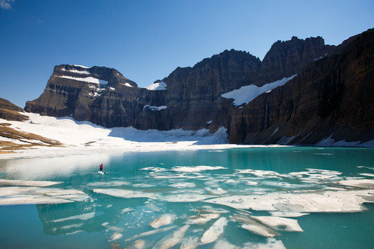 A woman stand up paddles (SUP) among floating chunks of ice on Upper Grinell Lake next to the remnants of the Grinell Glacier in Glacier National Park, Montana.